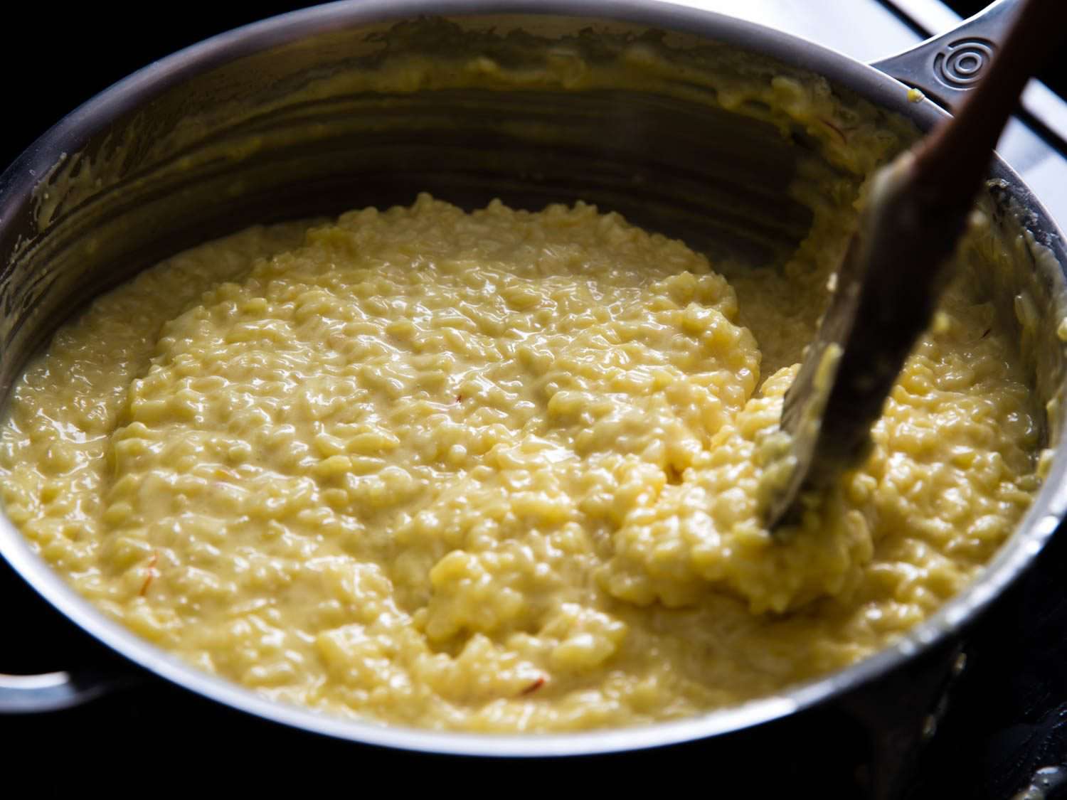 A pot of risotto alla Milanese is stirred with a wooden spoon as it finishes cooking.