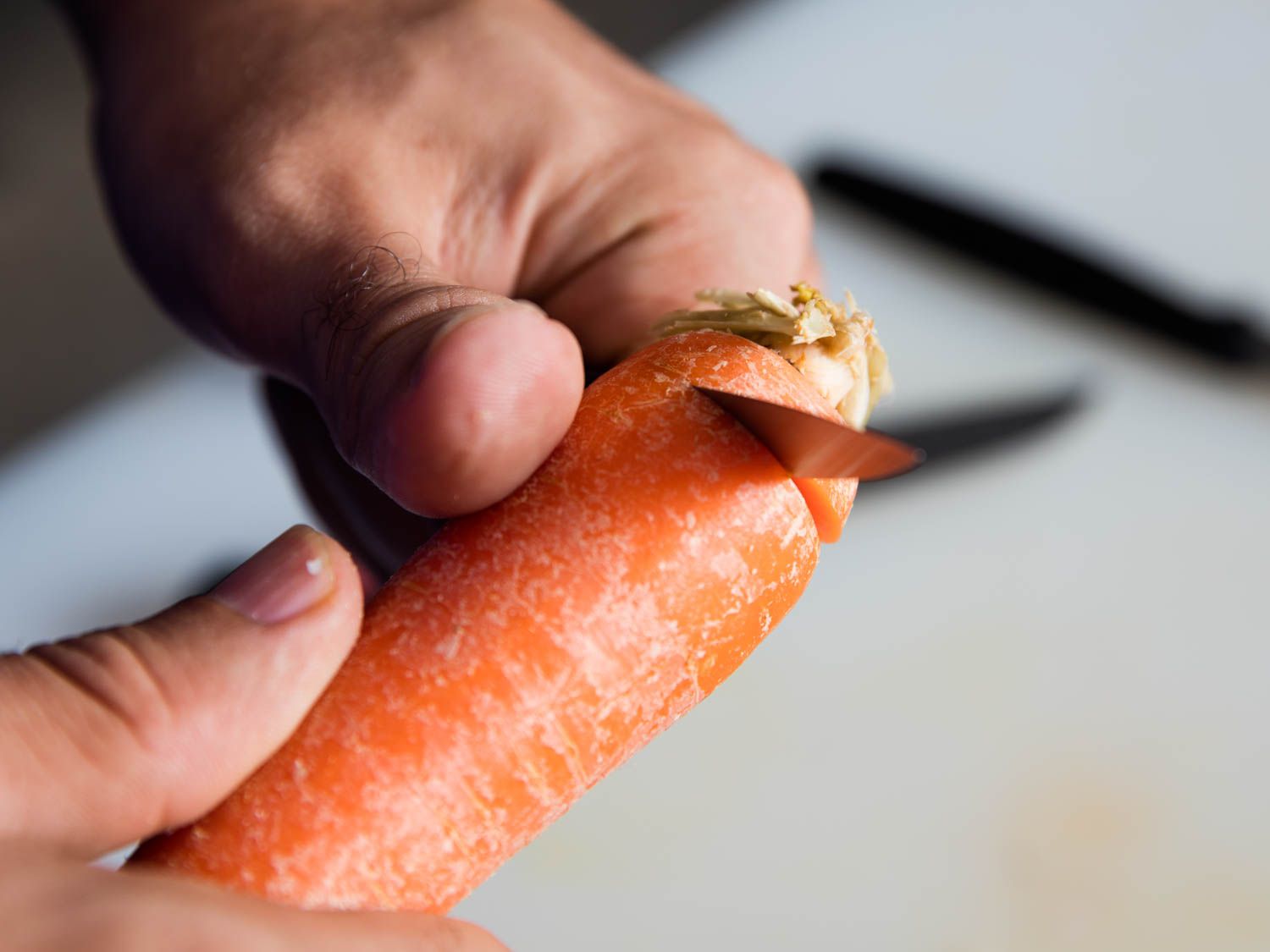 A pairing knife cutting off the top end of a carrot