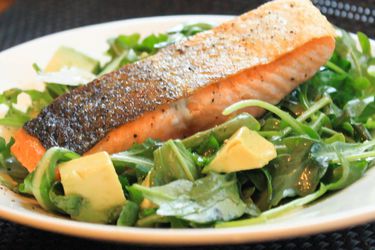 A piece of pan-roasted salmon plated on bed of arugula salad with avocado chunks