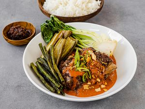 Bowl of kare kare set next to ramekin of shrimp paste and serving bowl of white rice