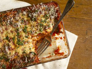 一个长方形的玻璃砂锅，里面装满了烤好的全美帕尔玛干酪茄子，切出一角的正方形，叉子放在盘子里。