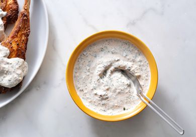 Yogurt mint sauce in a yellow bowl with a spoon, with sauce-covered meat on the left hand border of the image.