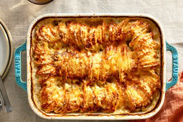 Browned hasselback potatoes in a blue stoneware baking dish on a linen tablecloth.