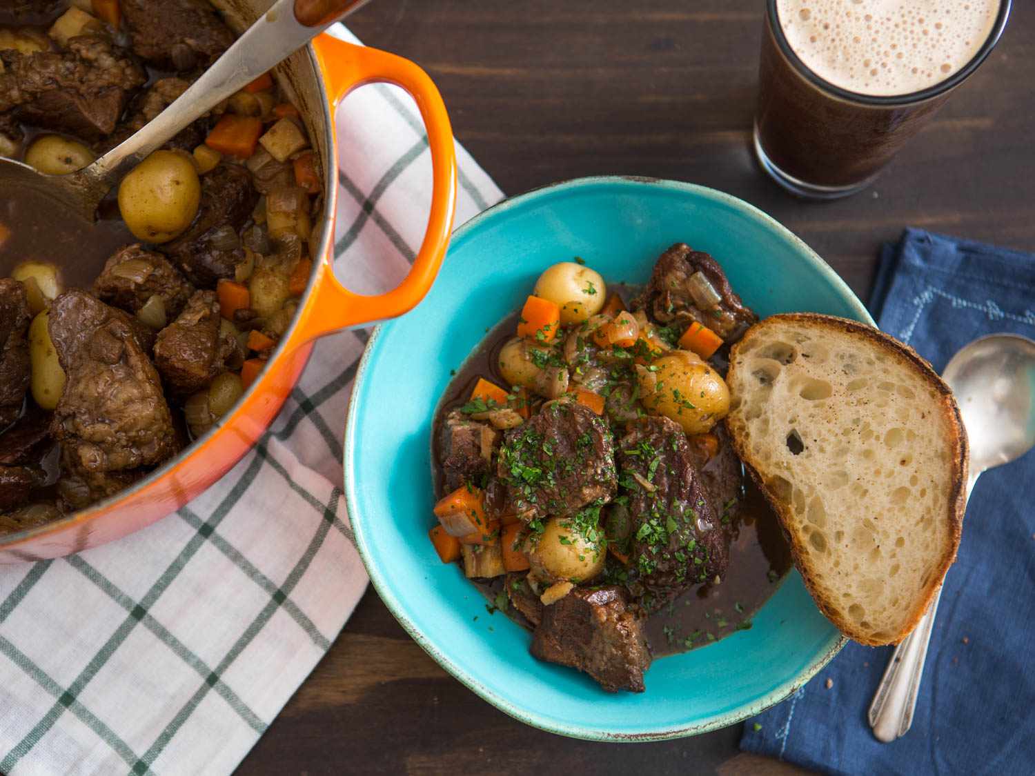 Overhead shot of a bowl of Irish Guinness Beef Stew dished out from a Dutch oven and served with a slice of bread and pint of Guinness ale