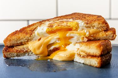 两个半烤奶酪蛋洞三明治摞在一起，奶酪和鸡蛋从中间溢出来。
