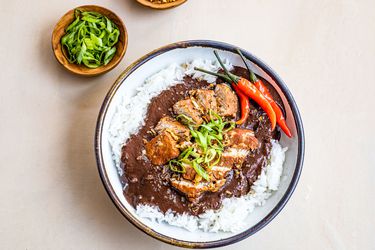 Dinuguan served over bowl of rice, garnished with chiles and sliced scallions