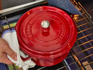 two hands removing a red Dutch oven from an oven rack