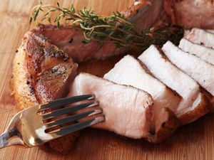 切好的带骨头的煮猪排，放在砧板上切成片。叉子在一片里。猪肉片旁边有一小枝新鲜的百里香。