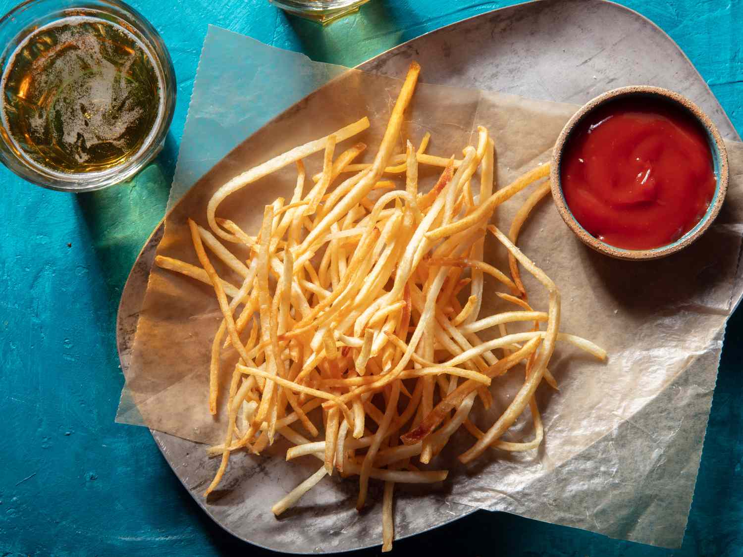 头顶上的观点shoestring fries on wax paper on a platter with a ramekin of ketchup and a glass of beer alongside