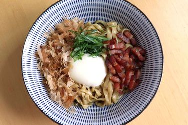 Closeup of bacon and egg mazemen, served in a patterned ramen bowl.