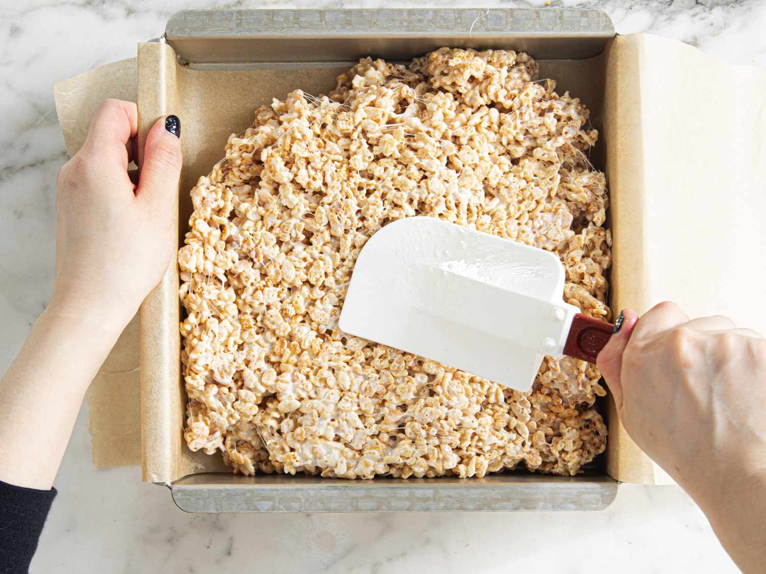 Smoothing rice krispies treat mixture into a baking pan with a silicon spatula