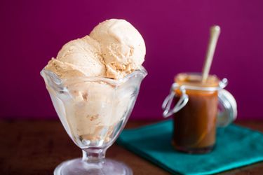 A parfait glass holding three scoops of cajeta ice cream with a small jar of cajeta in the background.