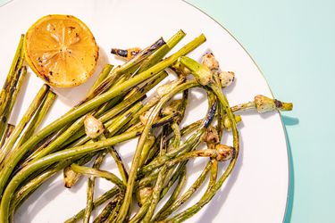 Grilled Garlic scapes on a white plate with a lemon