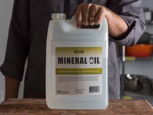 Hand holding a large jug of mineral oil on a wooden counter