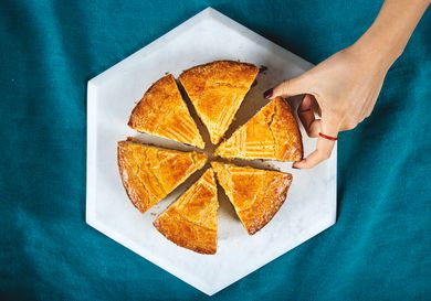 Overhead view of a sliced gateau basque cake with a hand reaching in for a slice