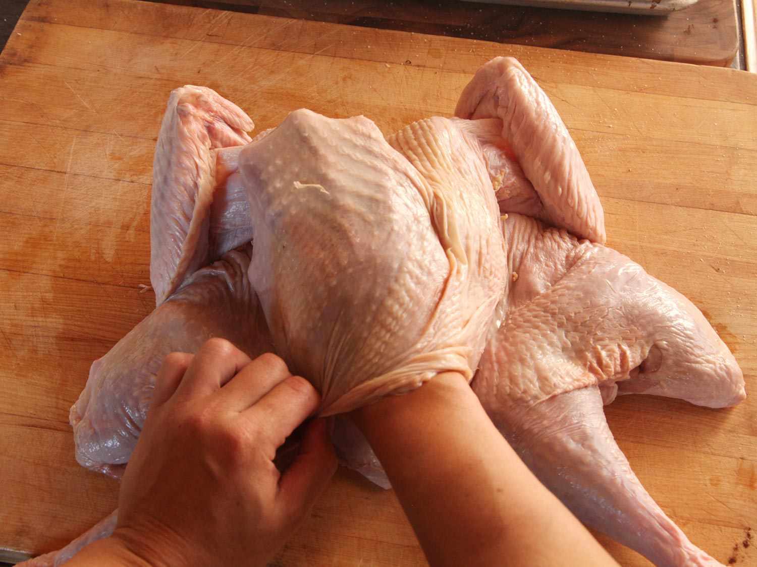 一只手将未煮熟的火鸡皮与火鸡分开，这样黄油就可以分布在火鸡皮下面。