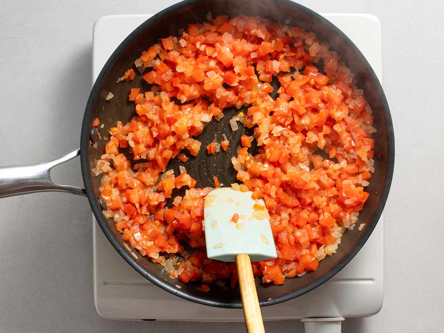 在不粘锅中煮洋葱和番茄并用硅胶铲搅拌。