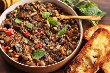 Overhead view of caponata, served in a wide bowl with toasted slices of ciabatta.