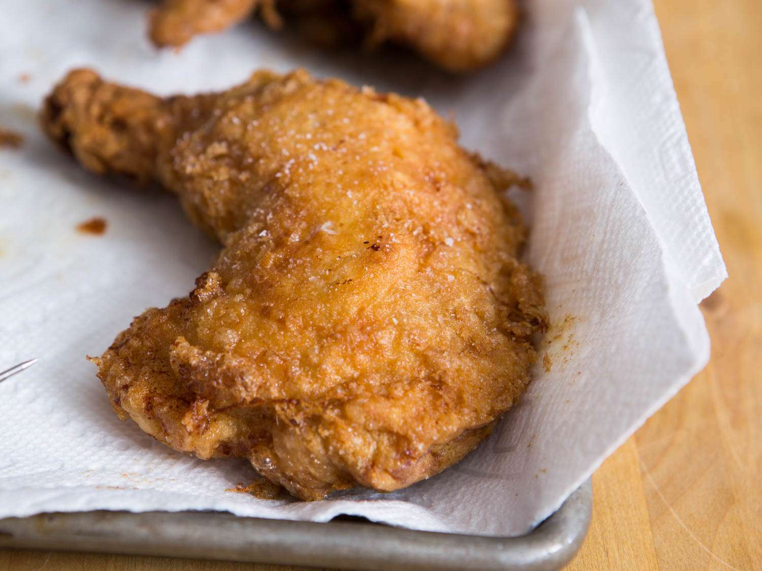Fried chicken resting on paper towels set in a rimmed baking sheet