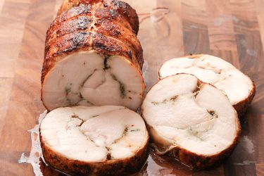 Roast turkey porchetta (turchetta) sliced and on a wooden cutting board.