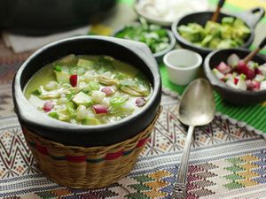 A bowl of green pozole verde topped with avocado and radish