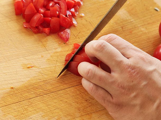 一只手把成熟的番茄稳稳地放在砧板上，把它切成小块