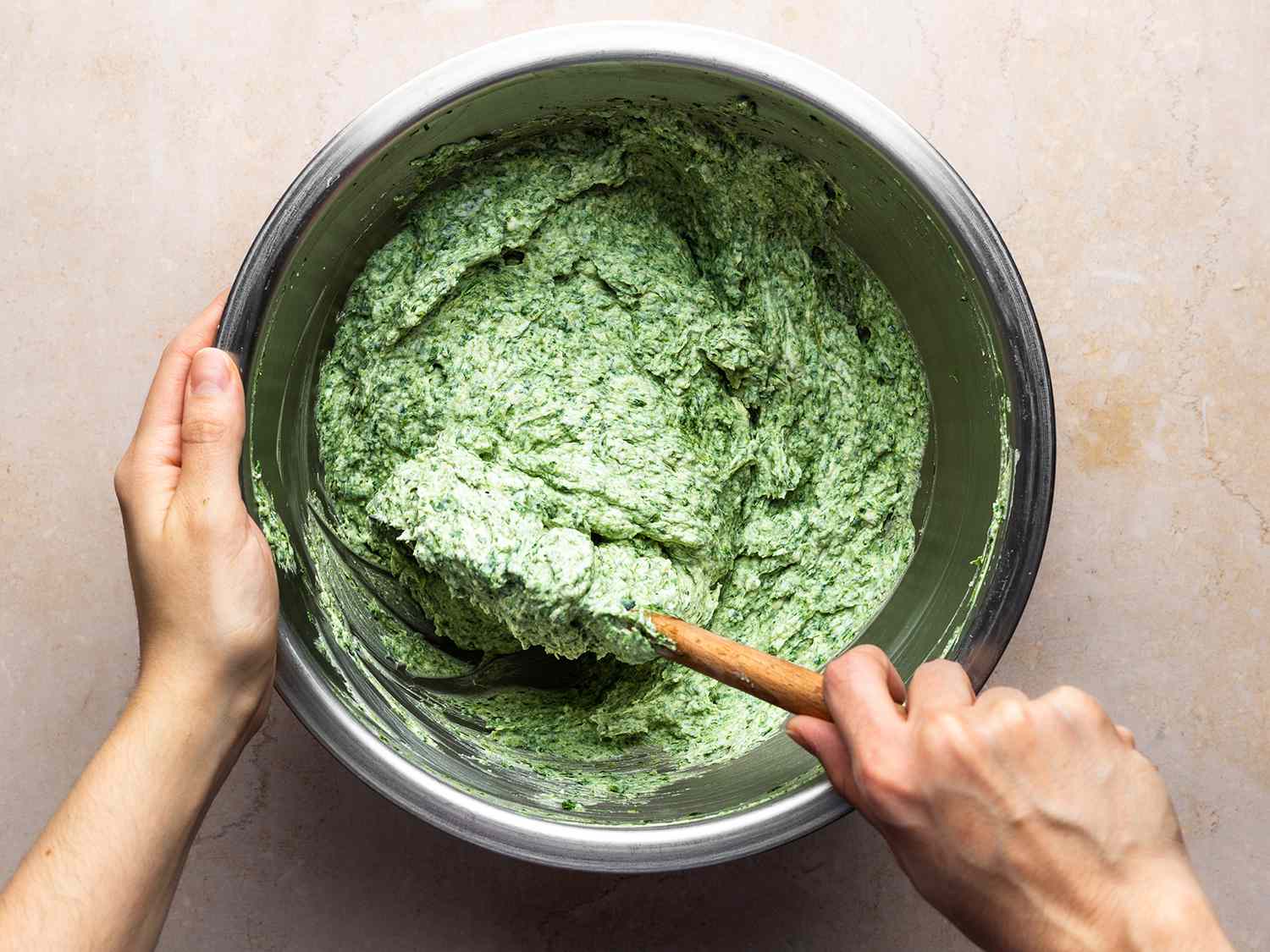 The ricotta being mixed with cooked and processed spinach in a metal bowl.