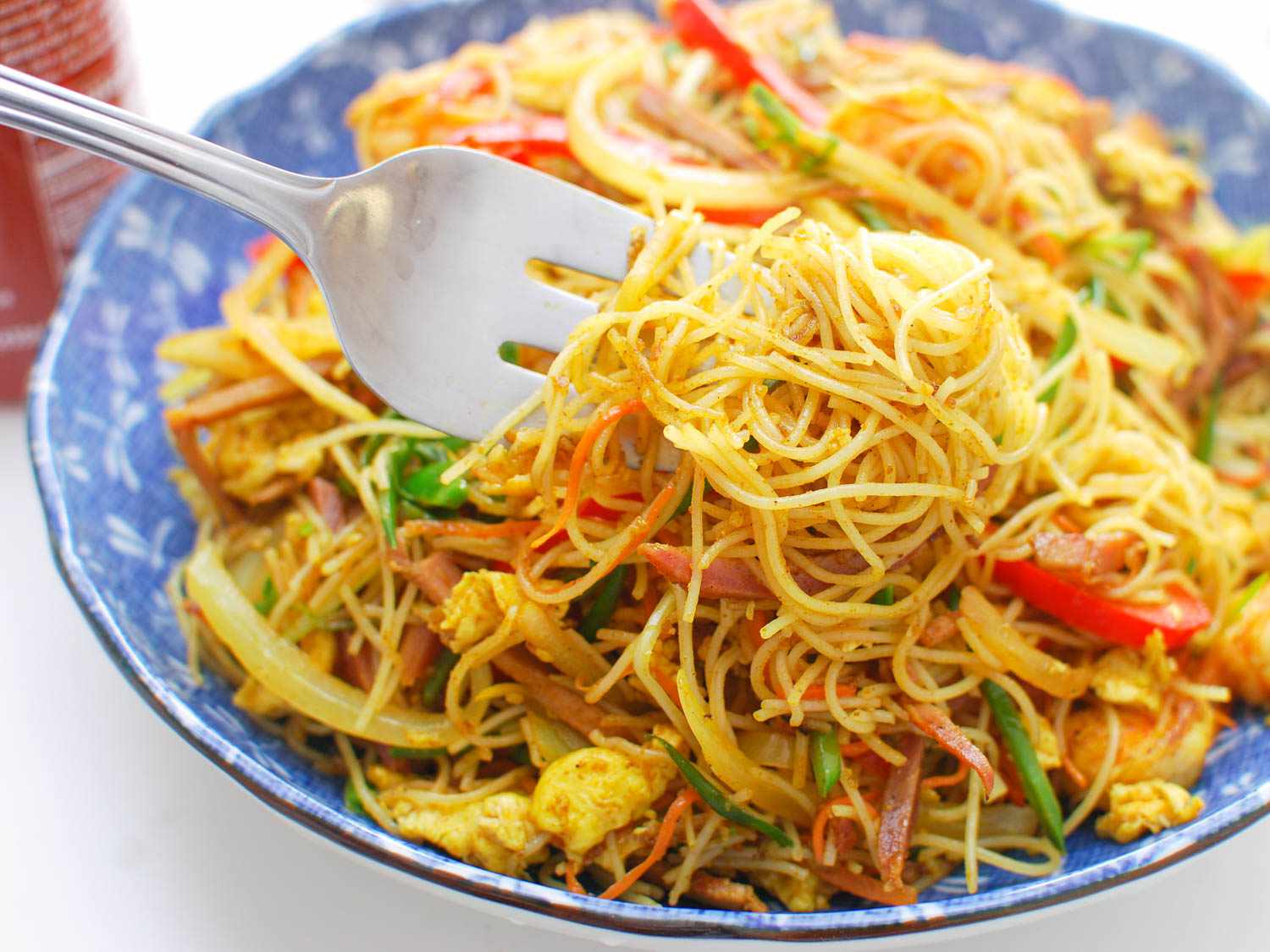 A fork twirling Singapore rice noodles from a bowl.