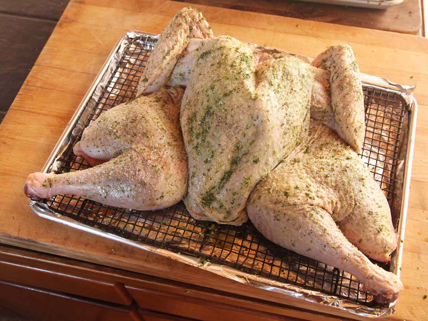 一只未煮熟的整只烤火鸡，涂上融化的香草黄油，放在铁丝架上，烤盘上盖上锡纸。