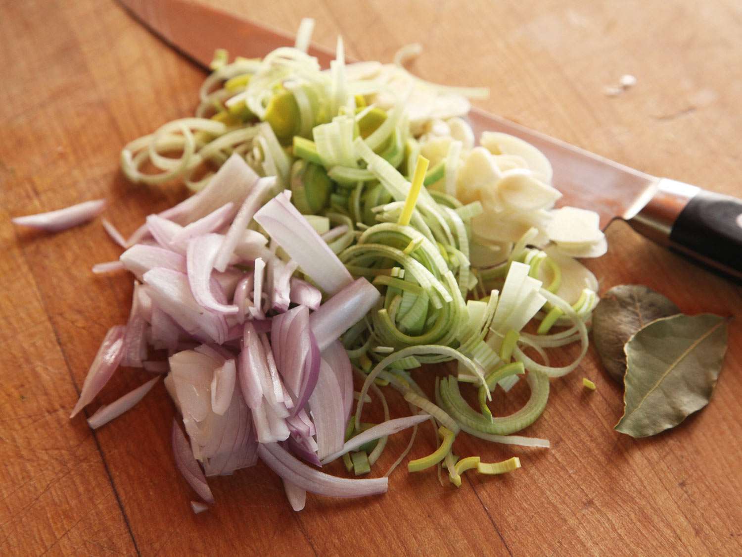 切成片的葱、韭菜和大蒜堆在砧板上，旁边放一对月桂叶。