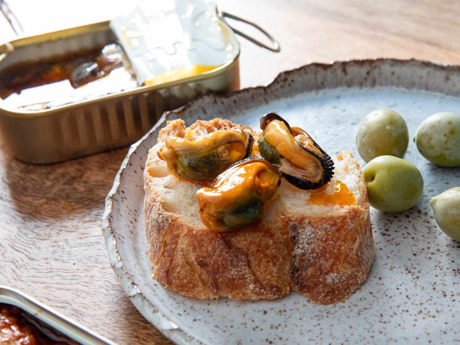 Close up of mussels in escabeche on a piece of baguette with some olives on a plate