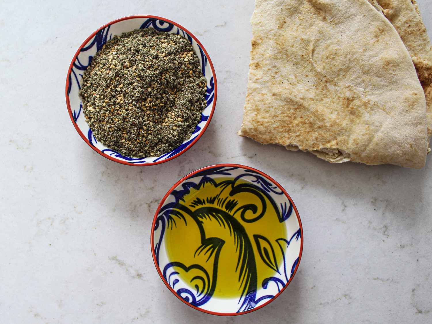 Za'tar in a small bowl next to a piece of pita and a small shallow bowl of olive oil