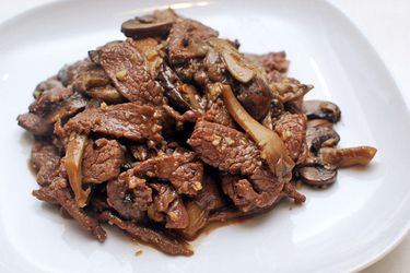 一个白色的盘子里放着一堆炒牛肉和蘑菇。