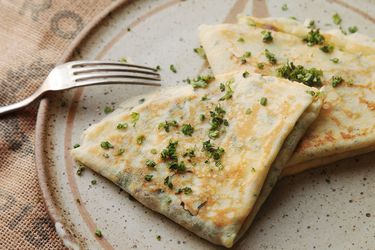 Two quarter-folded filled crepes garnished with chopped herbs on a plate