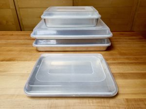 a stack of sheet pans with lids on them with one sheet pan in front