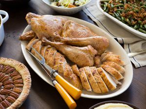 A platter of carved turkey with a carving knife and fork, surrounded by pecan pie, green bean casserole, and salad.