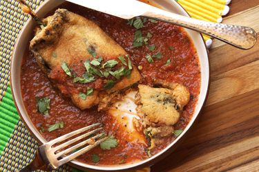 Overhead of chiles rellenos, a stuffed and fried pepper on a bed of roasted tomato salsa