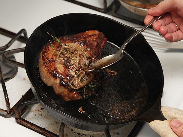 在铸铁煎锅里涂上烤好的猪排，上面撒上葱头和百里香