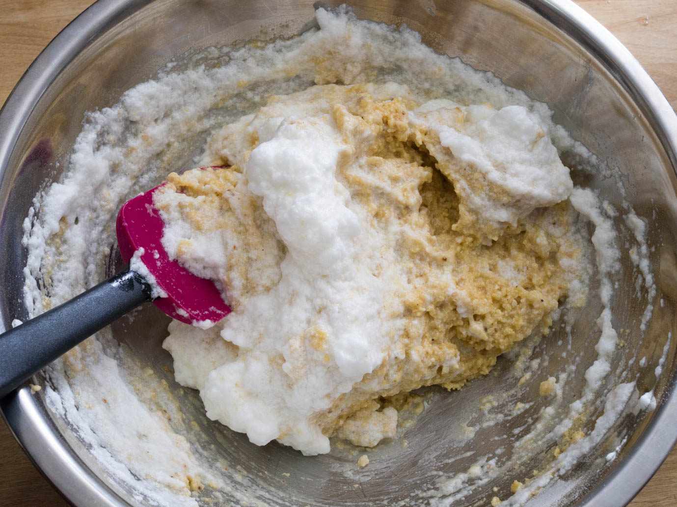 Overhead close-up of beaten egg whites being folded into a bowl of matzo-ball mixture with a silicon spatula.
