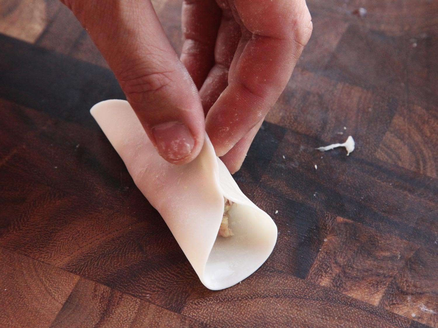 把饺子皮的两边捏在一起。在饺子皮的中间有碎猪肉和卷心菜馅。