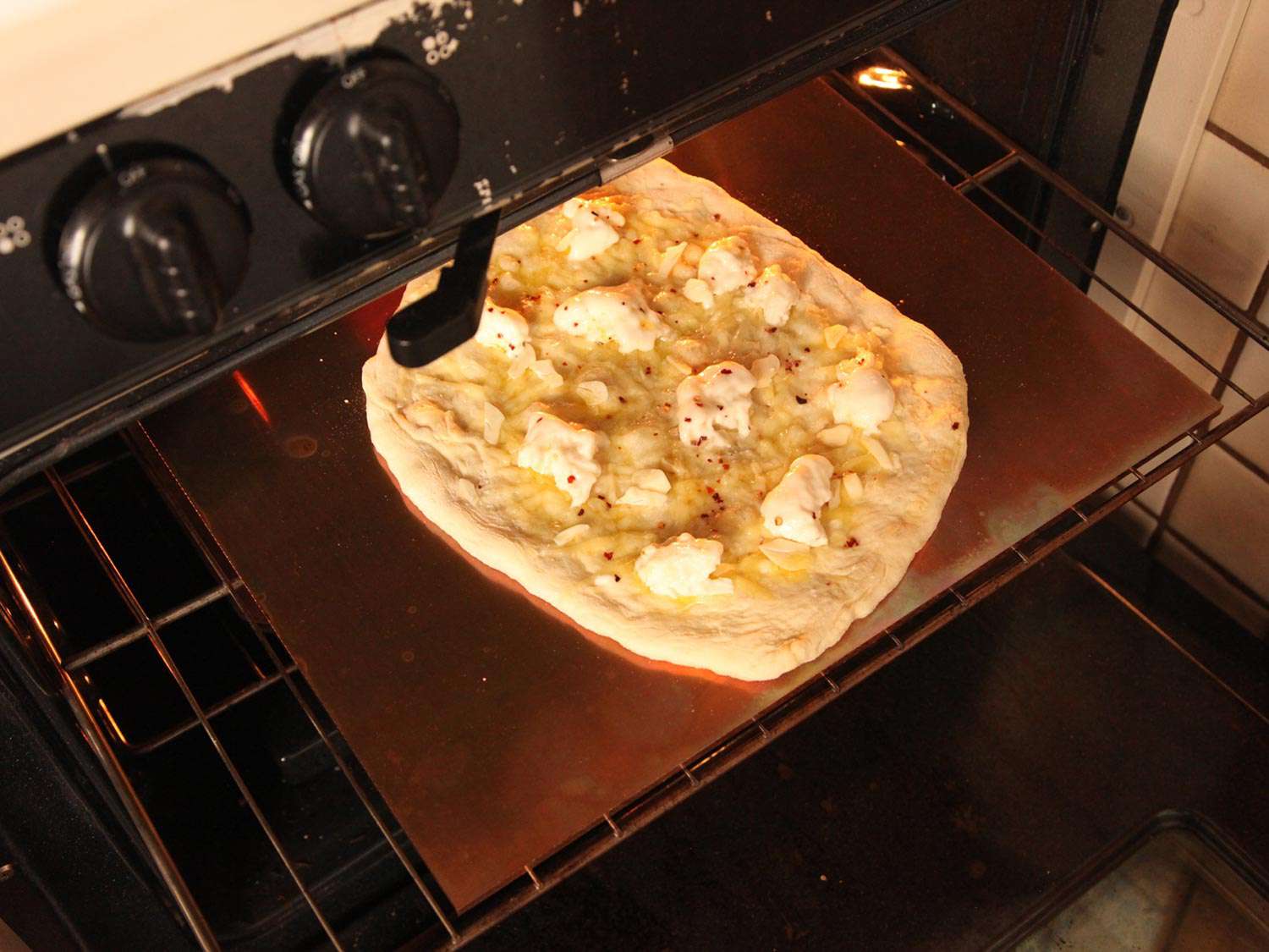 披萨面团上面撒着撕碎的马苏里拉奶酪和Gruyère碎放在烤盘上准备放进烤箱。
