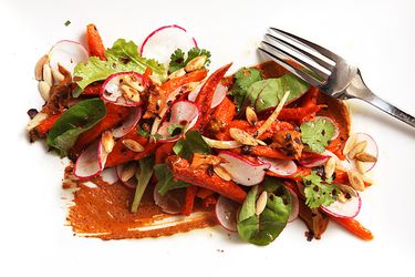 Closeup of roasted carrot salad with peanut-sesame mole, served on a white plate.