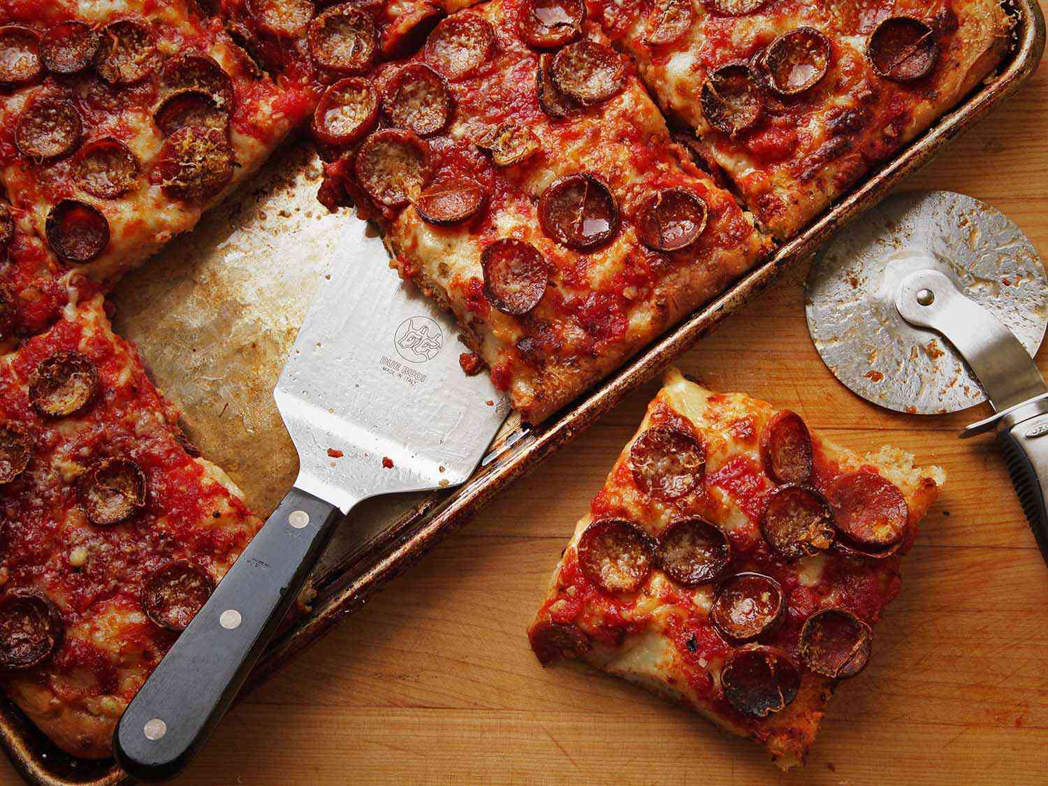 在有边的烤盘里放一片意大利辣香肠披萨，旁边是一片完整的披萨