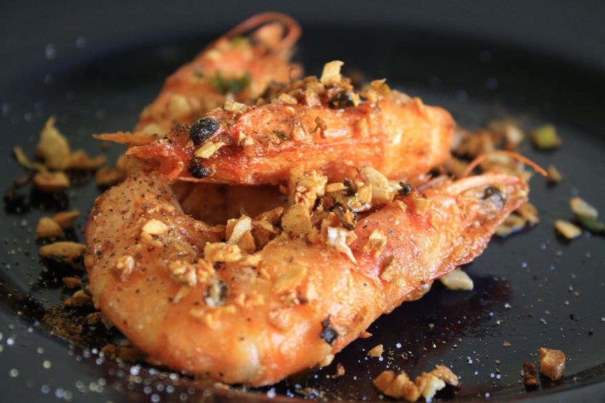 两个中式炸咸虾的特写，上面裹着棕色的大蒜、葱花和辣椒片。