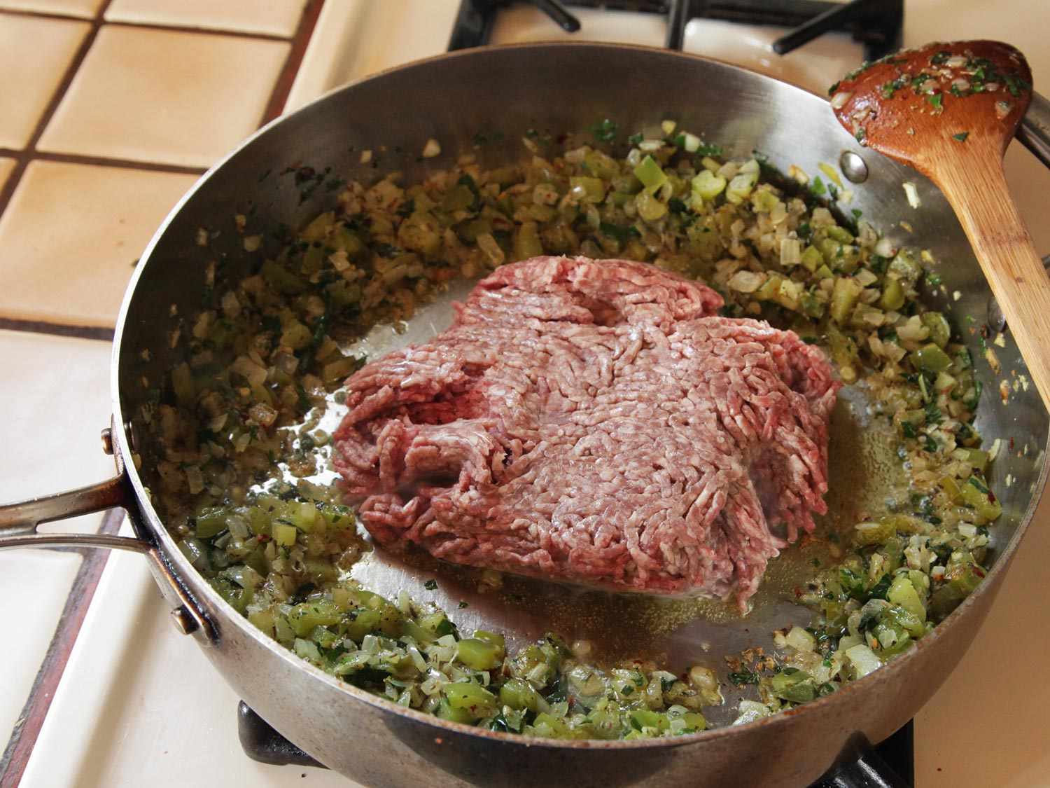 洋葱、青椒和香料被推到锅的边缘，为一大堆生碎牛肉腾出空间。