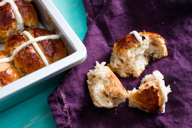 A spiced vanilla hot cross bun, torn into several hunks, is perched on a purple velour cloth next to the pan it was baked in.