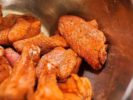 把生鸡翅放在搅拌碗里，然后涂上卡津香料混合物。