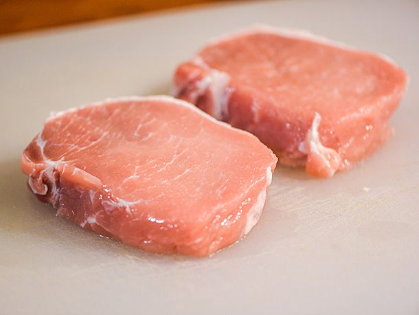 Two slices of pork loin on a plastic cutting board.