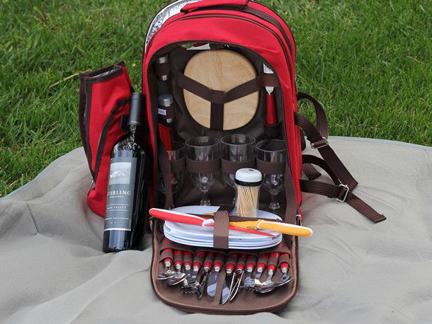 一个红色的野餐背包里面有牙签、盘子、杯子和餐具，还有一瓶酒。