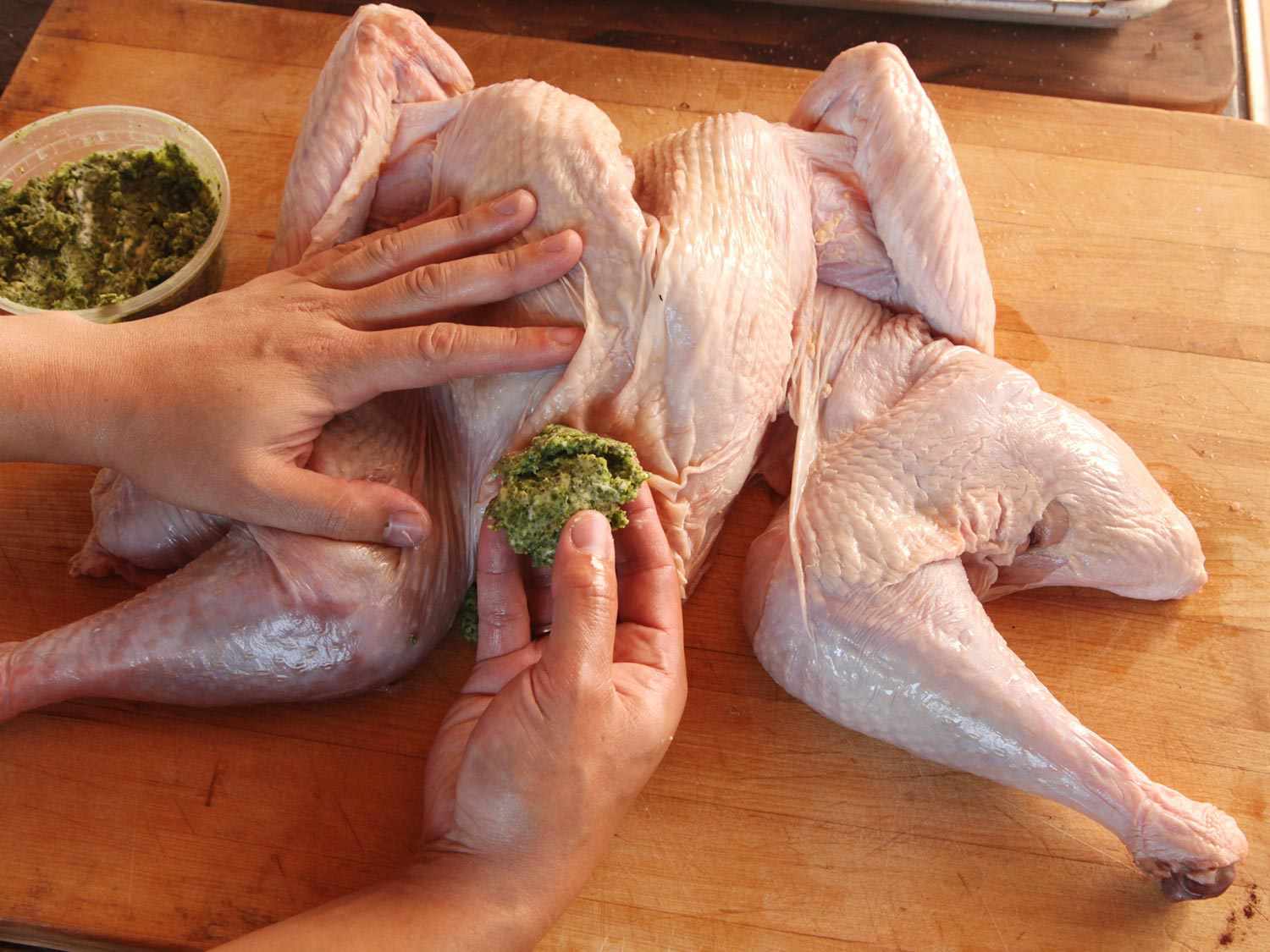 一只手拿着一只未煮熟的火鸡，另一只手拿着一大块香草黄油，准备插入皮肤下面。